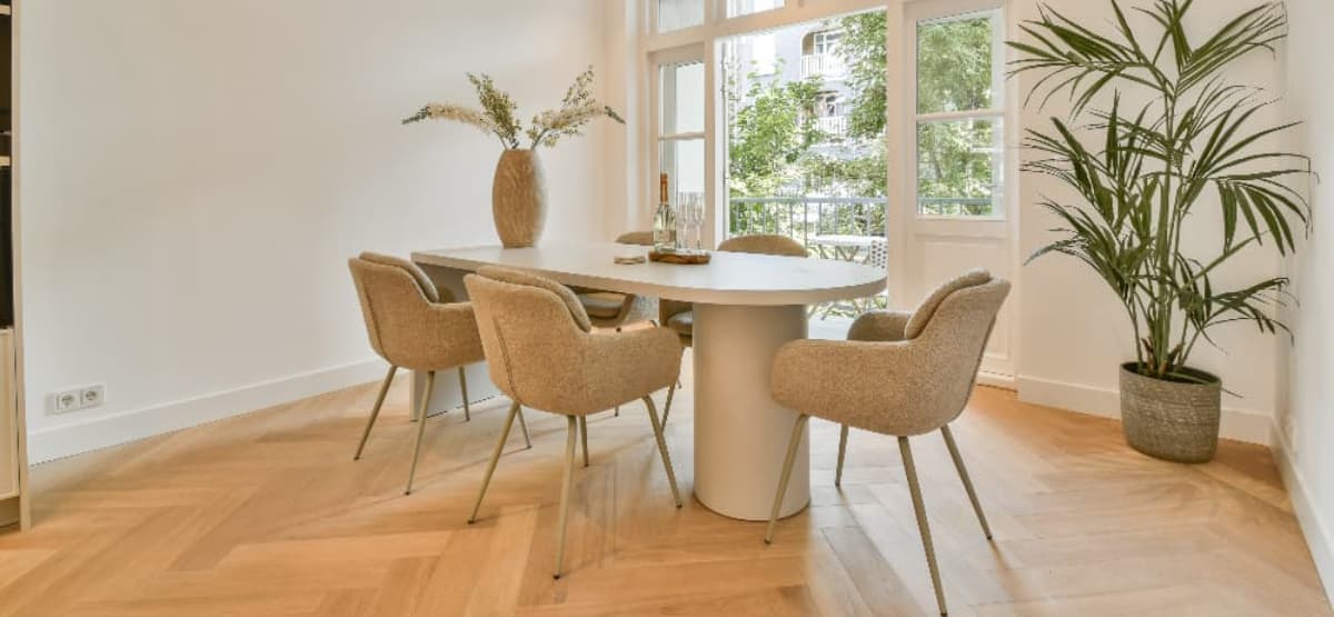 Bright modern dining room with a round table, upholstered chairs, wooden flooring and large windows letting in natural light