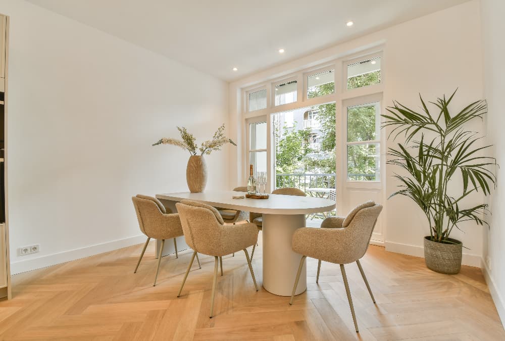 Bright modern dining room with a round table, upholstered chairs, wooden flooring and large windows letting in natural light