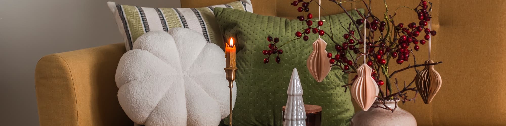 Mustard sofa with cushions and a wooden coffee table decorated with berries, ornaments and a lit candle.