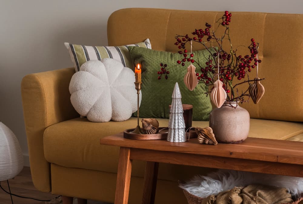 Mustard sofa with cushions and a wooden coffee table decorated with berries, ornaments and a lit candle.